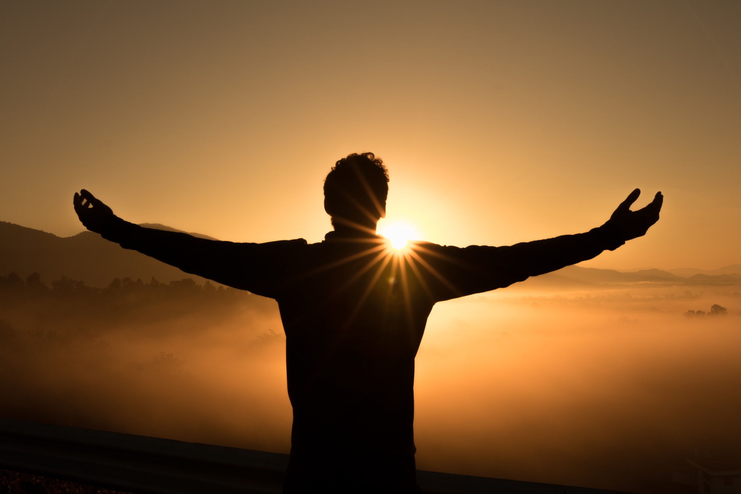 Young man, arms extended, at sunset, no longer feeling anxious after anxiety treatment using hypnotherapy.